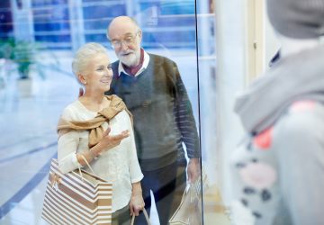 Retired couple standing by display window and discussing new collection of clothes