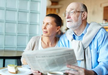 Modern couple of seniors with newspaper sitting in cafeteria